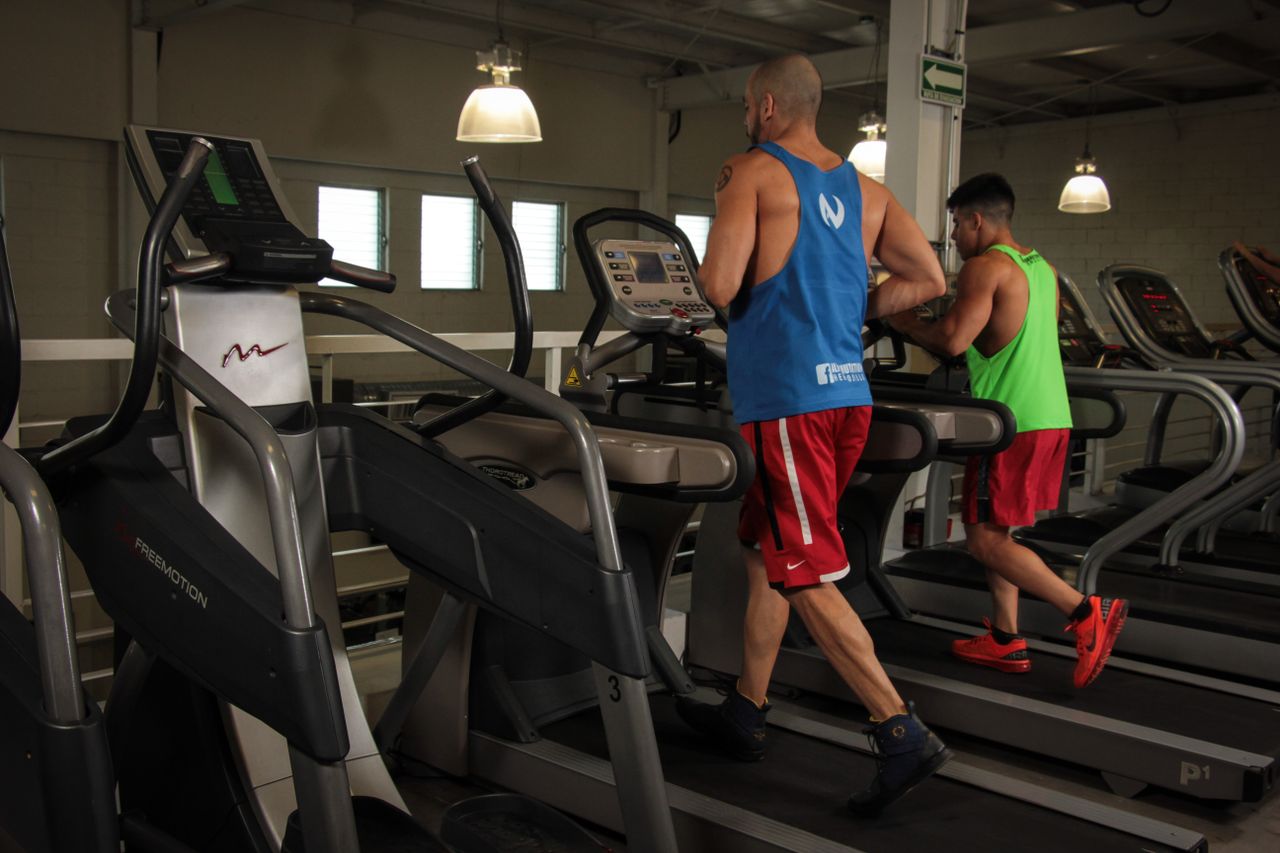 about-us-02 Two men running on treadmills in a modern gym, promoting fitness and health.
