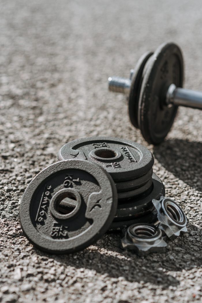 about-us-01 Adjustable dumbbells with weight discs left on asphalt sports ground in bright sunlight