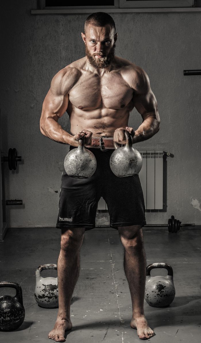 services-03 Shirtless man with muscular build lifting kettlebells indoors, showcasing strength and fitness.